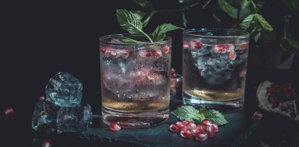 two colorful summer drinks with pomegranate and mint on a black table