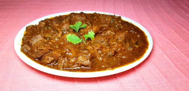 Chickin Tikka Curry in thick red gravy in white plat on light background.